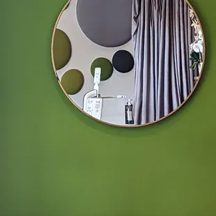 a circular mirror hanging on a green wall