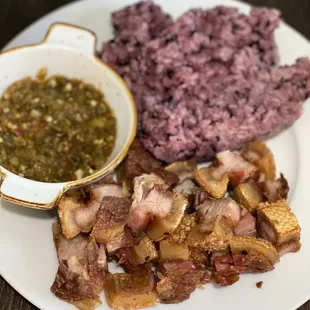 a plate of meat, rice, and a bowl of sauce