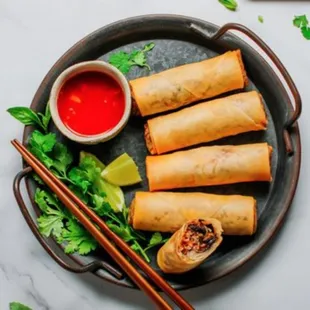 a plate of fried spring rolls with dipping sauce and chopsticks