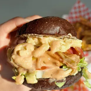 a hand holding a hamburger with macaroni and cheese