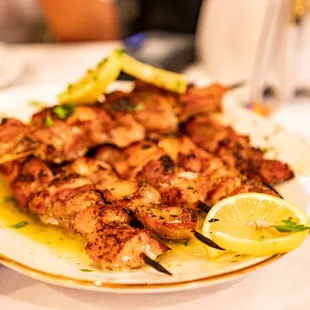 a plate of chicken skewers with lemon wedges