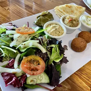 Delicious vegetarian plate with falafel, pita, dolma, green salad, hummus, baba ghanoush, and tzatziki