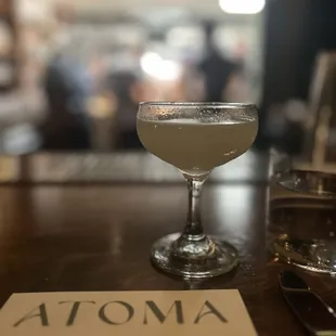 Aviator cocktail with Atoma menu and a blur of kitchen activity behind.