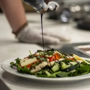 a plate of salad being drizzled with dressing