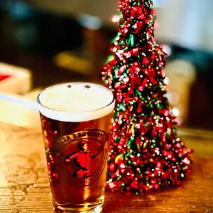 a glass of beer next to a christmas tree