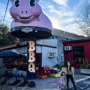 a woman and a child standing in front of a pink pig