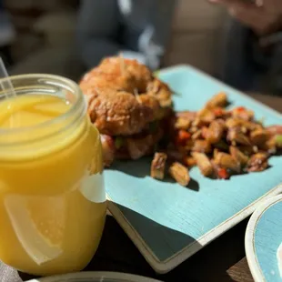 Delicious OJ and a bacon egg croissant and country style potatoes