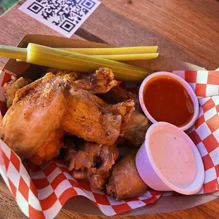 a basket of chicken wings with a pickle and sauce