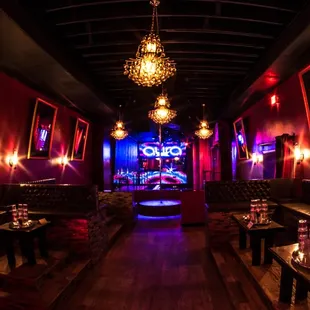 a dimly lit bar with red walls and black leather booths