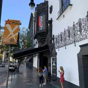 two people standing on the sidewalk in front of a building