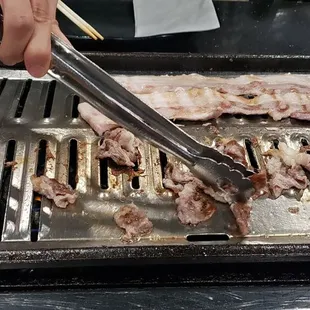 a person using tongs to cut meat on a grill