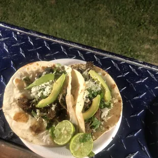 Carne asada tacos topped with onion, cilantro, queso fresco and avocado slices