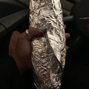 a hand holding a sandwich wrapped in aluminum foil