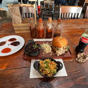 Pork sandwich with slaw, dirty rice and beans, and their four sauces. From right to left: hot, ginger tabasco, regular, sweet.
