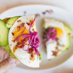 a hand holding a sandwich with an egg and pickled onions