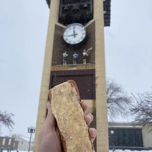 a person holding a donut in front of a clock tower