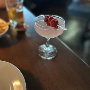 a closeup of a cocktail with a raspberry garnish