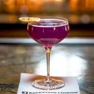 a purple cocktail in a coupe glass