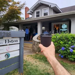 a person holding a cup of coffee in front of a house