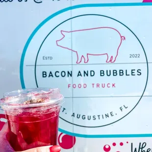 a person holding a drink in front of a food truck