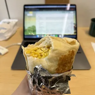 a person holding a burrito in front of a laptop