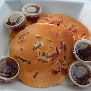 Half stack of bacon pancakes to-go with syrup.