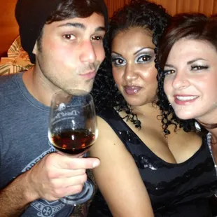 three people posing for a picture with a glass of wine