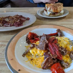 Scrambled eggs in foreground, corned beef hash, bagel sandwich in background