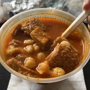 a hand holding a spoon over a bowl of stew