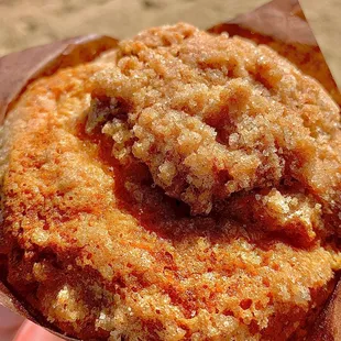 a hand holding a muffin with a crumb topping