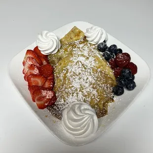 a plate of food with strawberries, blueberries, and powdered sugar