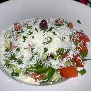 a plate of salad with tomatoes, cucumbers and parmesan cheese