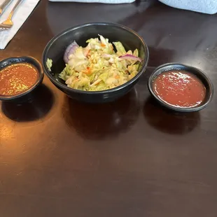 a bowl of salad and two small bowls of sauce