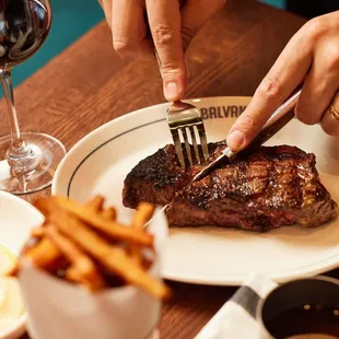 a person cutting a steak with a fork