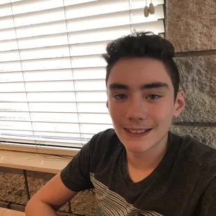 a young man sitting at a table with a pizza in front of him