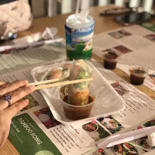 a person holding chopsticks over a tray of food