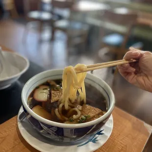 a person holding chopsticks over a bowl of noodles