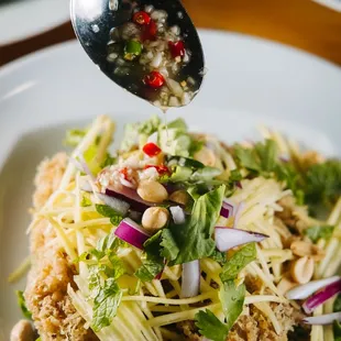 a spoon drizzing a salad with peanuts