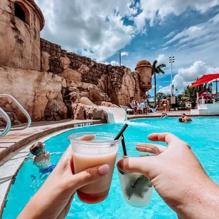 two people holding drinks in front of a pool