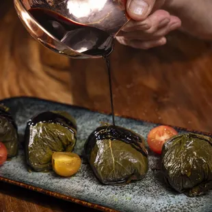 a person pouring wine over a plate of stuffed grape leaves