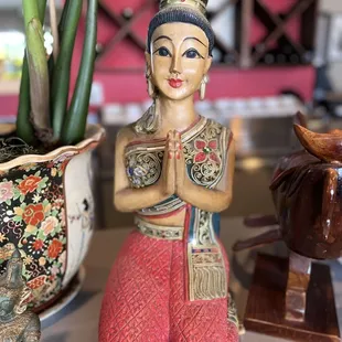 a statue of a woman praying in front of a potted plant