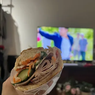 a person holding a sandwich in front of a tv