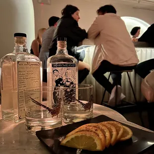 people sitting at a bar with bottles of gin and orange slices