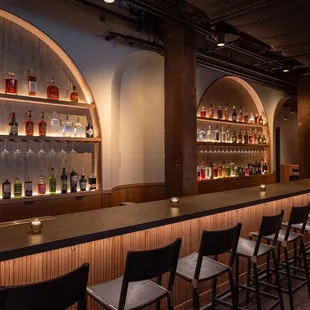 a row of bar stools in front of a row of liquor bottles