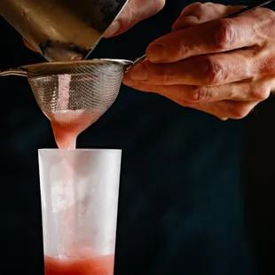 a person pouring a drink into a glass
