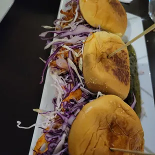 three burgers on a plate with pickles