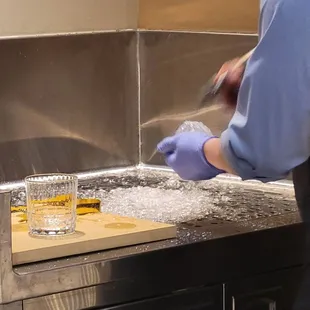 a man in a blue shirt and blue gloves pouring ginza into a glass