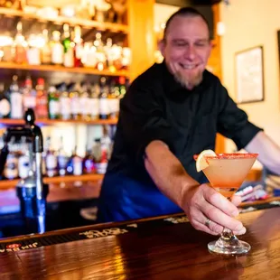 a bartender at a bar holding a cocktail