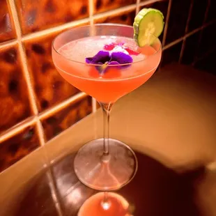 a pink cocktail with a purple flower garnish