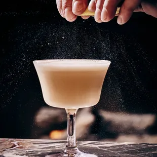 a person sprinkling sugar on a cocktail glass